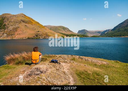 Eine Frau sitzt am Ufer des Crummock Water im Lake District, Cumbria, England, und genießt den Blick über das Wasser und den umliegenden Berg Stockfoto