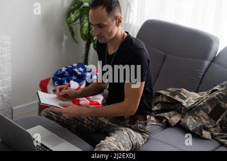 Patriotischer Militärangehöriger im Headset, der in der Nähe der amerikanischen Flagge auf einen Laptop schaut Stockfoto