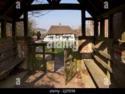 Das Hampshire Dorf Hampshire. Der reetgedeckte Red Lion Pub wird durch die Litschentore der Pfarrkirche St. Michael und All Angels gesehen. Stockfoto