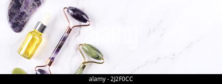 Banner mit Gesichtsmassage-Kit - Amethyst und Jade gua Sha Werkzeug und Gesichtswalzen mit Beauty Face Serum, kosmetisches Öl auf weißem Marmor Hintergrund mit Stockfoto