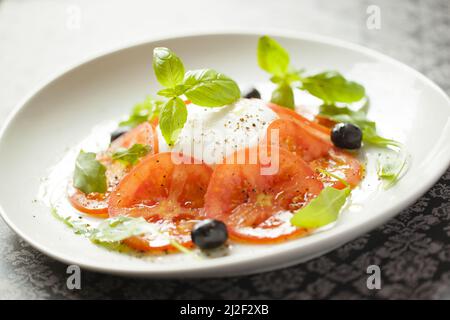 Eine Nahaufnahme eines Caprese-Salats mit Tomaten und Mozzarella-Käse auf einem weißen Teller Stockfoto