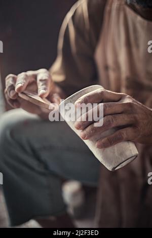 Der Künstler poliert raue Kanten eines Keramikköpfen mit einem Schwamm im Töpferstudio. Stockfoto