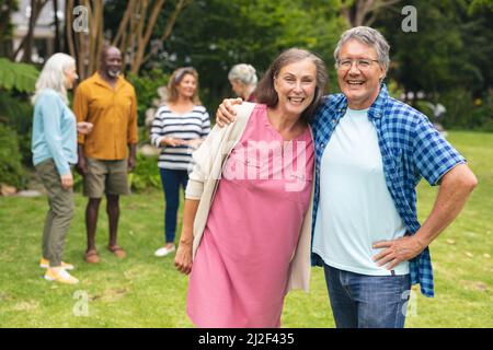 Porträt eines glücklichen kaukasischen älteren Paares mit multirassischen Freunden im Hintergrund Stockfoto