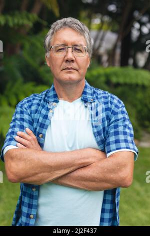 Porträt eines selbstbewussten kaukasischen älteren Mannes mit gekreuzten Armen und einer Brille im Hinterhof Stockfoto