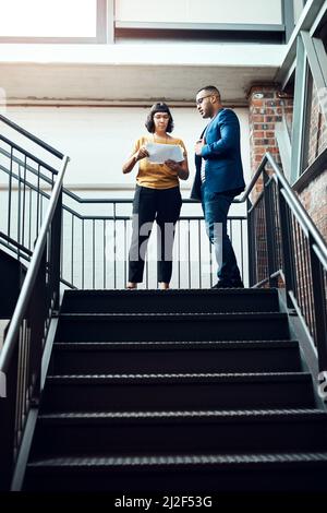 Bringen vielfältige und dynamische Ideen zusammen. Aufnahme von zwei Designern, die eine Diskussion über eine Treppe in einem Büro führen. Stockfoto