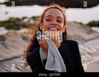 Yoga schwitzt. Aufnahme einer attraktiven jungen Frau, die nach einer Yoga-Sitzung am Strand alleine stand und ein Handtuch benutzte. Stockfoto