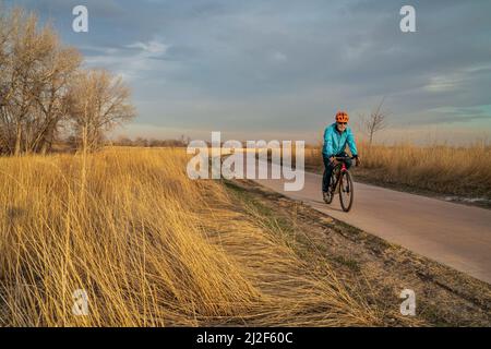 Am frühen Frühlingsnachmittag auf einem Radweg mit einem älteren Radfahrer, der auf einem Schotterrad fährt - Poudre River Trail in Fort Collins, Colorado Stockfoto