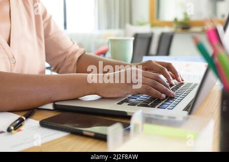 Mittelteil einer afroamerikanischen Freiberuflerin mit mittlerem Erwachsenen, die einen Laptop am Schreibtisch benutzt Stockfoto