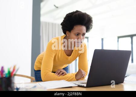 Seriöse afroamerikanische Freiberuflerin mit mittlerem Erwachsenen, die am Schreibtisch am Laptop arbeitet Stockfoto