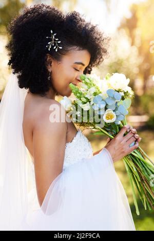 Der süße Geruch von Liebe und Glück. Aufnahme einer glücklichen und schönen jungen Braut, die an ihrem Hochzeitstag im Freien ihren Blumenstrauß riecht. Stockfoto