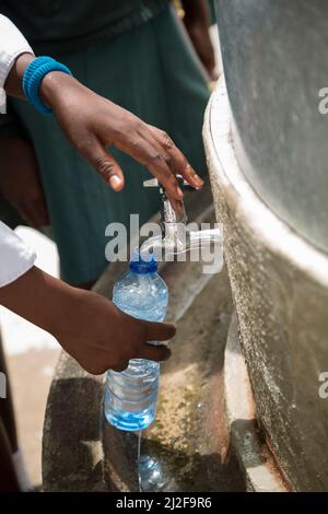 Schüler füllen nachfüllbare Plastikwasserflaschen aus einem Brunnen in ihrem Schulhof in der Oshana Region, Namibia, Afrika. Stockfoto