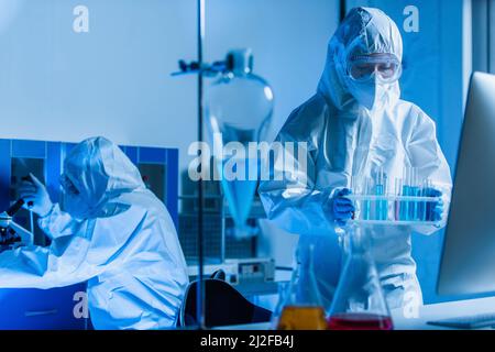 Bioingenieur hält Reagenzgläser, während Kollege am Hintergrund arbeitet, Stockbild Stockfoto