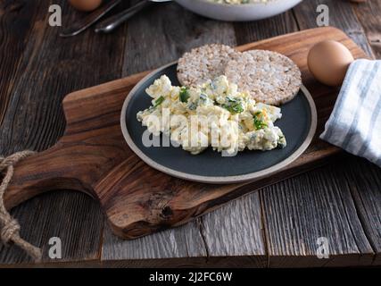 Proteinreicher Snack mit Quark, gekochten Eiern und Schnittlauch. Serviert mit braunem Reiskracker auf einem Teller Stockfoto