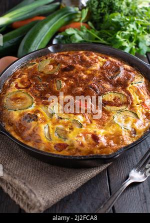 Im Ofen gebackene Frittata mit mediterranem Gemüse wie Zucchini, Tomaten, Paprika und roten Zwiebeln. Serviert in einer rustikalen gusseisernen Pfanne. Stockfoto