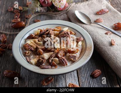 Porridge mit Pekannüssen, Datteln, Bananen, Äpfeln und Zimt auf rustikalem und Holztisch Stockfoto