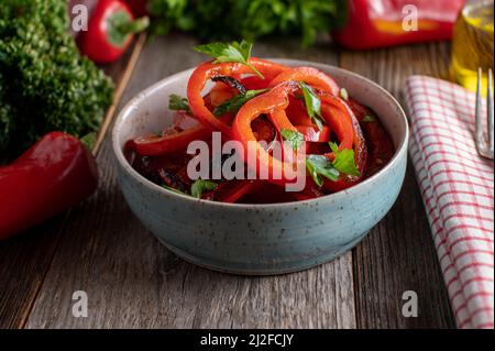 Gieße Olivenöl über einen gerösteten roten Paprikasalat Stockfoto