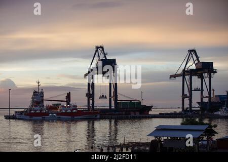 Die Abendsonne untergeht über Containerkranen, die am Hafen in Makassar, Indonesien, stehen. Stockfoto