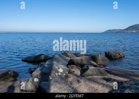 Felsbrocken als Teil eines Wellenbrechers in einem See. Bild vom See Vattern, Schweden. Blaues Wasser und Himmel im Hintergrund Stockfoto