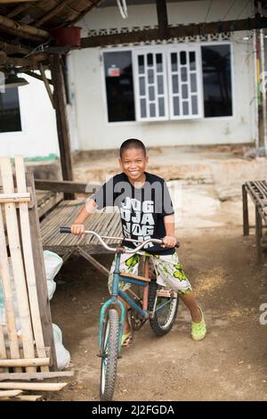 Ein lächelnder Junge fährt mit dem Fahrrad auf der kleinen abgelegenen Insel Karampuang, Indoneisa, vor der Küste von Mamuju, Sulawesi. Stockfoto