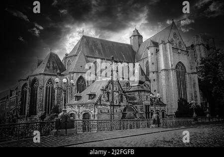 Schwarz-Weiß Vintage foto von alter Kopfsteinpflasterbrücke, mystischer mittelalterlicher gotischer Kirche, dramatischer Himmel mit Sturmwolken - St. Michaels, Gent, Belgien Stockfoto