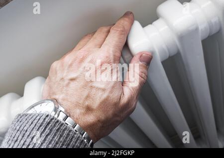 Männliche Hand berührt den weißen Heizkörper, Nahaufnahme mit selektivem Fokus. Moderne Haustechnik Stockfoto
