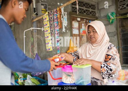 Eine Frau verkauft einem Kunden in ihrem kleinen Straßenstand auf der Insel Karampuang, Indonesien, Asien, einen Snack. Stockfoto