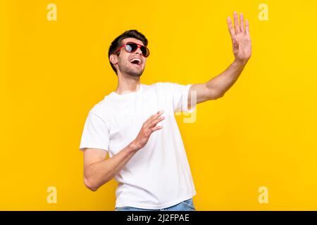 Foto von beeindruckt Millennial Brunet Kerl Tanz Welle tragen Brille T-Shirt isoliert auf gelbem Hintergrund Stockfoto