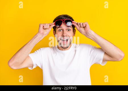 Foto von beeindruckt Millennial Brunet Kerl tragen Brillen weißen T-Shirt isoliert auf gelbem Hintergrund Stockfoto