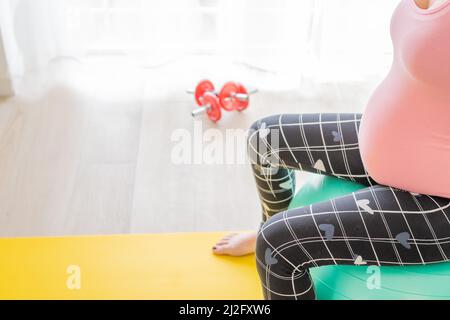 Junge, schwanger Frau, die auf einem Fitnessball sitzt und Sport macht, um in der Schwangerschaft aktiv zu bleiben Stockfoto