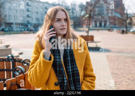 Verärgert junge 30s Frau sprechen auf dem Smartphone in der Frühlingsstraße fühlen sich beunruhigt enttäuscht von schlechten Nachrichten Stockfoto