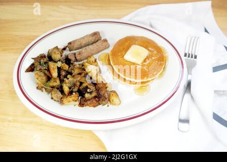 Eine Frühstücksmahlzeit mit Butterpfannkuchen, Wurstwaren Links und gebratenen Kartoffeln mit Rindfleisch Stockfoto