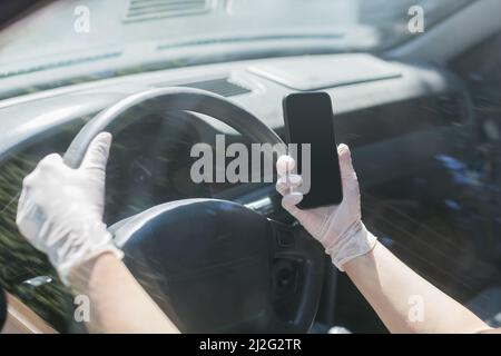 Auto mit Latexhandschuhen fahren und dabei ein Smartphone in der Hand halten Stockfoto