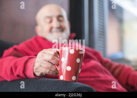 Alter Mann sitzt in einem Sessel und trinkt Kaffee Stockfoto