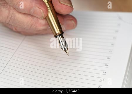 Goldfarbene Fontäne Tinte Stift in Senior Frau Hand über etwas auf leere tägliche Planer Seite schreiben, Nahaufnahme Detail Stockfoto