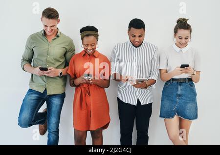 Aktualisierung unserer sozialen Medien. Ausgeschnittene Aufnahme einer vielfältigen Gruppe von Geschäftsleuten, die gemeinsam vor grauem Hintergrund stehen und Technologie im einsetzen Stockfoto