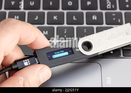 Galicia, Spanien; 1. April 2022: Hand hält eine Ledger Kryptowährung-Hardware-Wallet auf einem Laptop Stockfoto