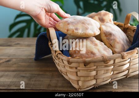 Die Hände der Frau legen hausgemachtes Pita-Brot in einen Holzkorb auf einen alten Holztisch. Speicherplatz kopieren. Stockfoto