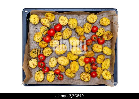 Gekochte Kartoffeln und rohe Kirschtomaten, die zum Backen auf einem Blech zubereitet werden, isoliert auf einem weißen Hintergrund mit einem Schneideweg, Draufsicht. Stockfoto