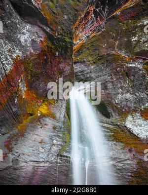 Ein fallendes kristallklares Wasser, das aus den farbigen felsigen Bergen herauskommt Stockfoto