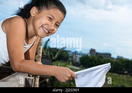 Schöne braune Latina Mädchen mit einem großen Lächeln, auf einem Holzbalkon winken die Friedensflagge. Glückliches Mädchen mit einer weißen Flagge in der Hand. Co Stockfoto