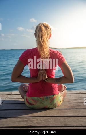 Kaukasische Frau, die an der Küste an einem Pier Yoga praktiziert Stockfoto