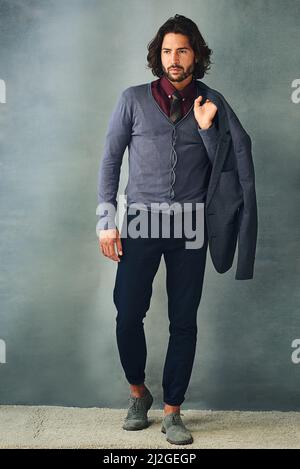 Kleidung macht den Mann. Studioaufnahme eines stilvoll gekleideten, hübschen jungen Mannes mit seiner Jacke über der Schulter. Stockfoto