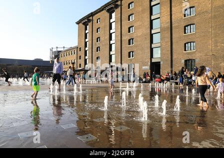 Kinder spielen in der Frühlingssonne in den Springbrunnen des Granary Square in Kings Cross, Nord-London, Großbritannien Stockfoto
