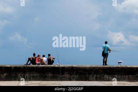 Der Mensch steht beim Angeln, während andere mit Angelstöcken an der Küste von Malecon sitzen und hoffen, den Fang des Tages in Havanna, Kuba, zu fangen. Stockfoto