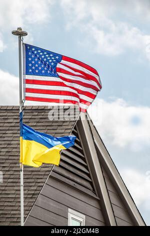 Ukrainische Flagge unter amerikanischer Flagge am windigen Tag im Wohnhaus - Nahaufnahme Stockfoto