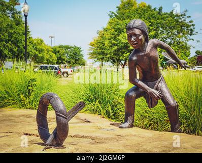 2021 07 20 Tulsa OK USA - Bronzestatue des amerikanischen Jungen, der mit Reifen und Darts auf Naturstein mit hohem Gras in städtischer Umgebung spielt Stockfoto