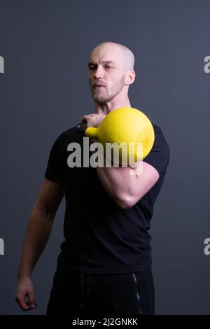 Typ mit einer gelben Kettlebell Fitnessstudio anonyme Trainingsstärke, von sportlichen Anstrengungen von Männern und Gummi Gewichtheben, südöstliche Aktivität. Gesunde Biegung Stockfoto