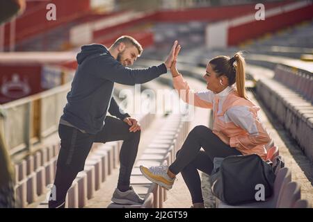 beardy-Typ und schöne weibliche geben sich im Stadion in Sportswear High-Five, lächelnd Stockfoto