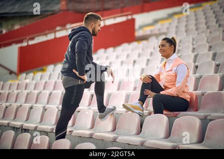 kaukasischer bärtiger Kerl und schöne Frau, die im Stadion sprechen, einander sehen und lächeln Stockfoto