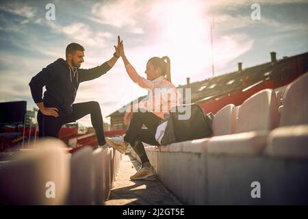 Zufriedener bärtiger Kerl und schöne weibliche geben sich High-Five nach erfolgreichem Training, lächelnd Stockfoto